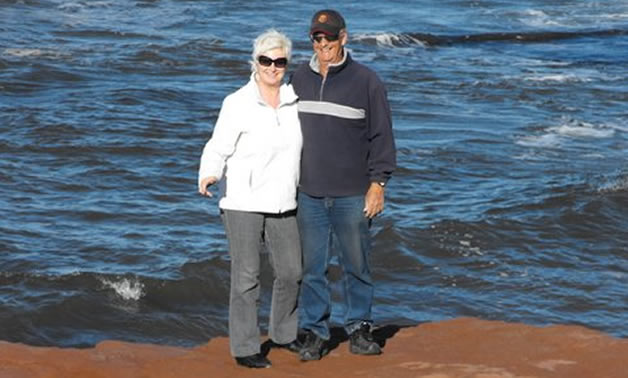 A man and woman wearing blue and white sweaters stand in front of the ocean.
