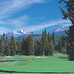 Scenic picture of the golf course in the forground, trees, mountains and ski in the background.