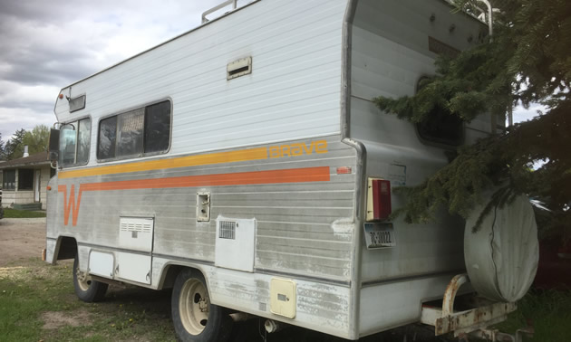 Winnebago motorhome with orange and yellow 'Flying W' logo on side, rear view.