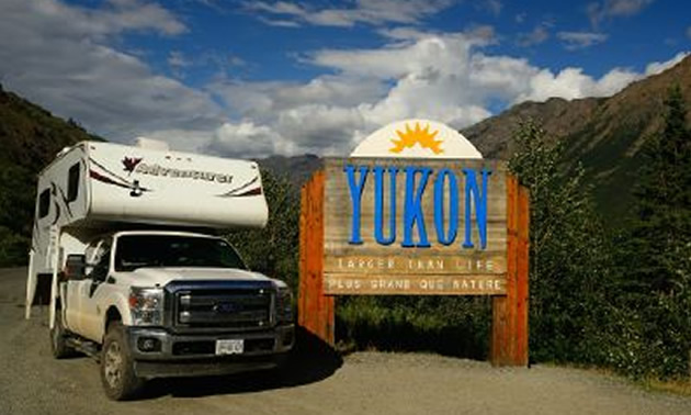 Truck camper parked beside sign.
