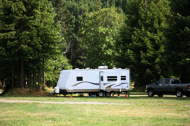 Picture of a  white RV trailer parked in a field with some trees behind it.