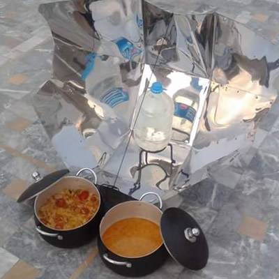 The solar cooker is sterilizing water and two cooked stew dishes are in front.