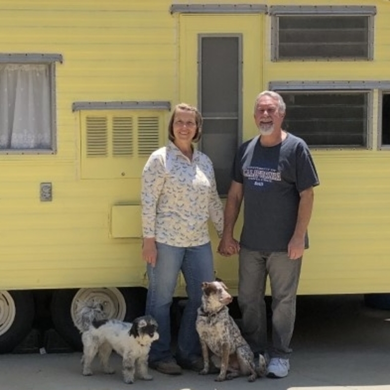 Couple with two dogs standing in front of a yellow vintage RV
