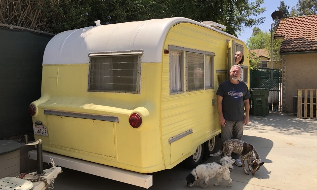 a couple with two dogs standing outside a yellow vintage Ken Craft trailer