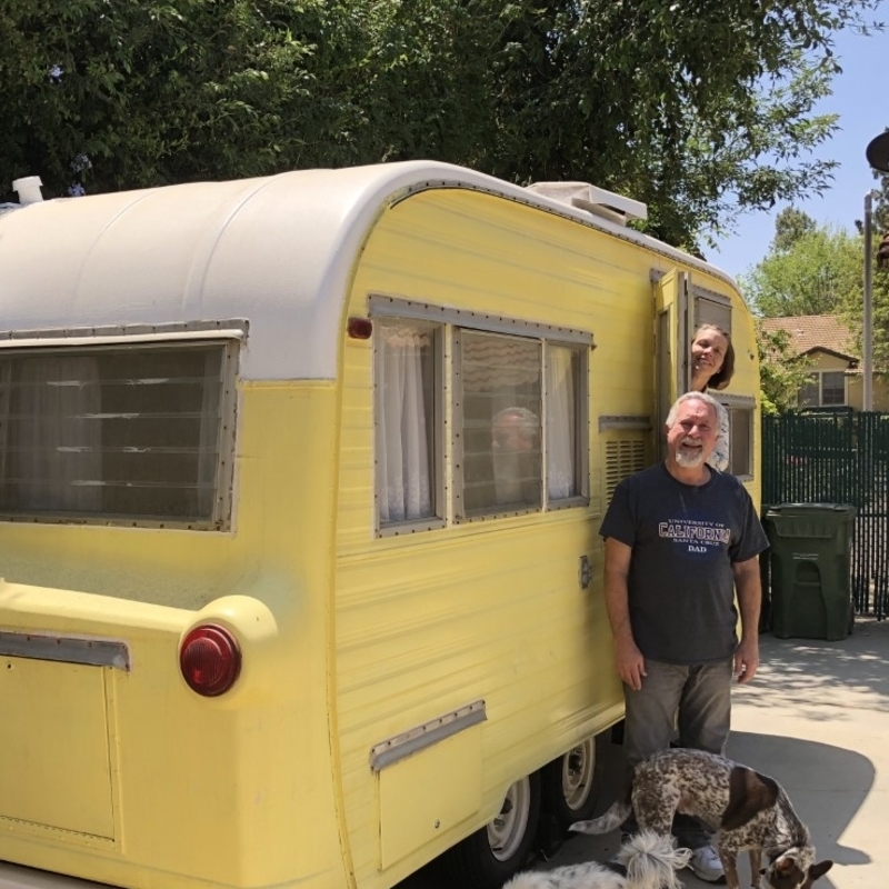 a couple with two dogs standing outside a yellow vintage Ken Craft trailer