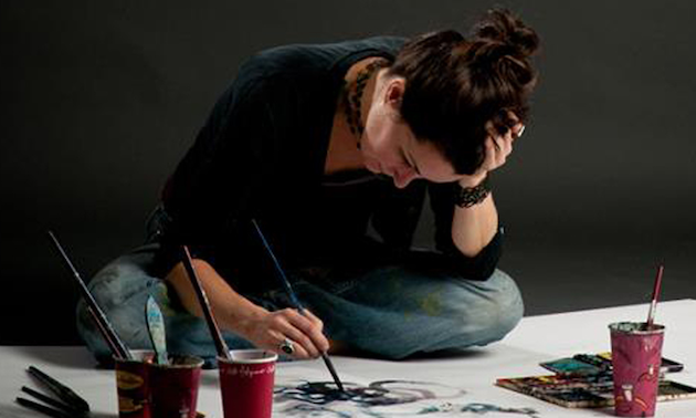 The artist Siobhan Humston sitting cross legged on the floor painting one of her pictures.