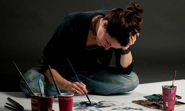 The artist Siobhan Humston sitting cross legged on the floor painting one of her pictures. 