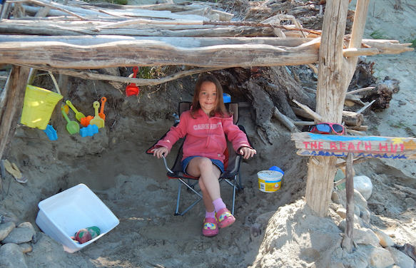 Kayden Gillard relaxing in a child sized lawnchair in a beach hut made out of drift wood. 