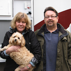 middle-aged couple standing in front of RV; woman holding a dog.