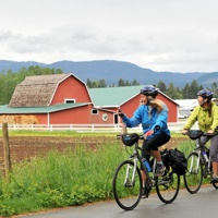 2 Bikers riding past a red barn.