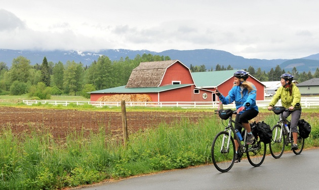 2 Bikers riding past a red barn.