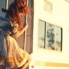 A young woman in a dress climbs down a ladder that is attached to the end of an RV.