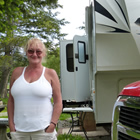 Photo of a lady in a white shirt standing in front of a red Dodge truck and a fifth wheel trailer. 