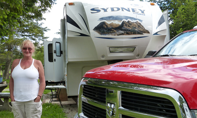 Photo of a lady in a white shirt standing in front of a red Dodge truck and a fifth wheel trailer. 