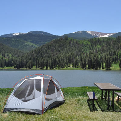 Scenic picture of tent, picnic table, with lake and mountains in background. 