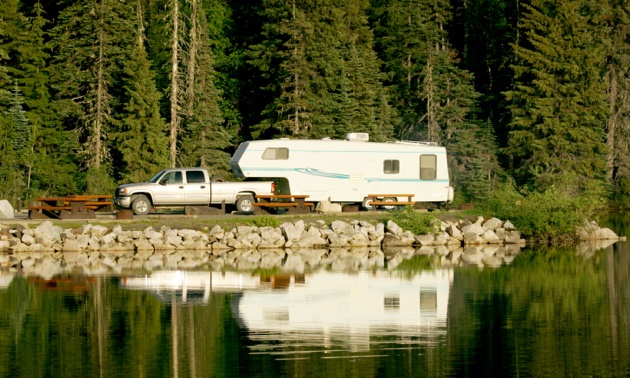 Truck pulling a trailer parked at a pristine, clear lake. 