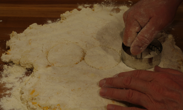 A person is cutting the dough with a biscuit cutter.