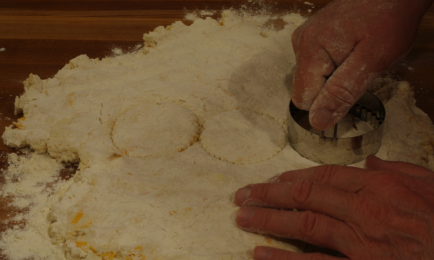 A person is cutting the dough with a biscuit cutter. 