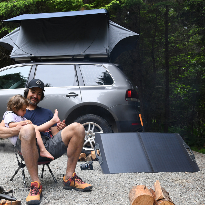A man and a child sitting together beside a camp stove an RV and a solar panel