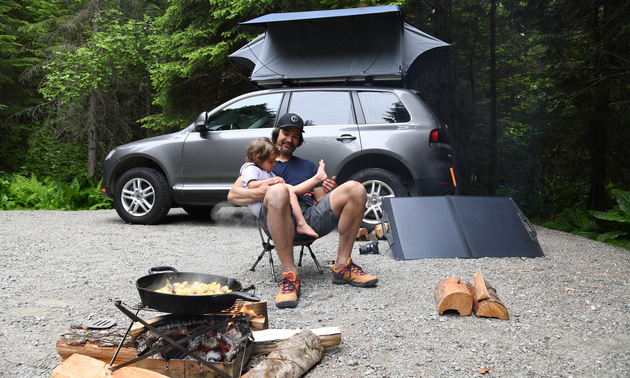 A man and a child sitting together beside a camp stove an RV and a solar panel