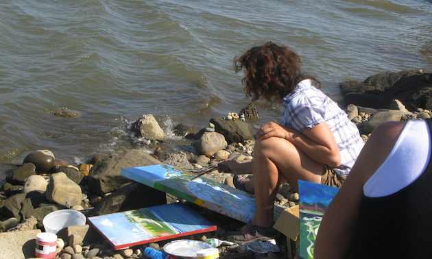 A woman painting beside a river.