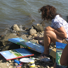 A woman painting beside a river.