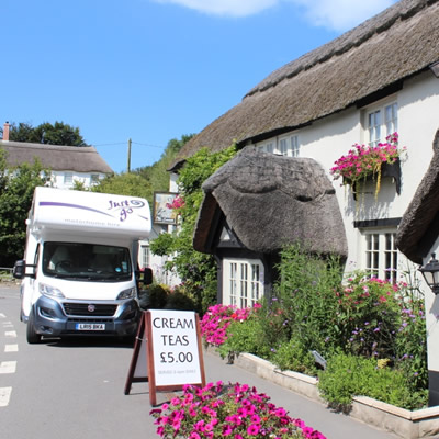 RV parked in front of quaint English thatched cottage. 