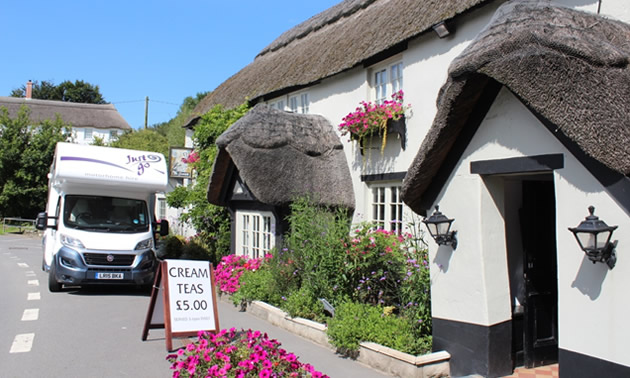 RV parked in front of quaint English thatched cottage.