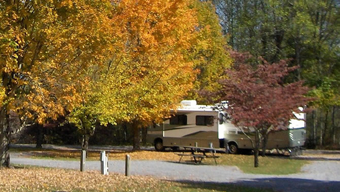 A picture of a RV parked at a campsite in the fall. 