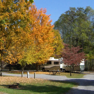 A picture of a RV parked at a campsite in the fall. 