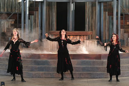 Three women in witch costumes perform on a stage.