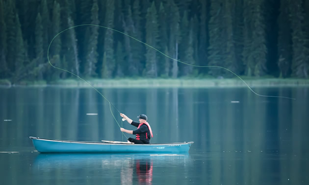 Peter Johnson sits in a canoe and casts into Fish Lake. White lines on the water surface are trout coming to the surface to eat flies.