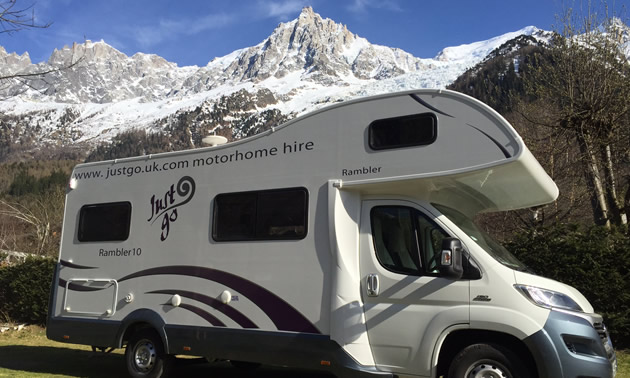 RV parked along side of road, with view of French Alps in background. 