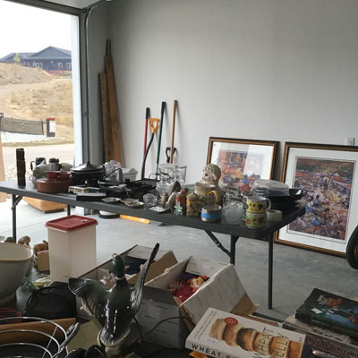 Open garage with table full of items for sale, large pictures leaning against wall. 