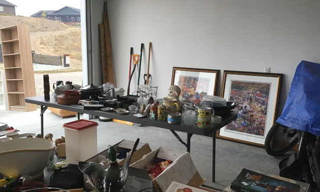 Open garage with table full of items for sale, large pictures leaning against wall. 