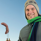 Man holding a barbecued hot dog on a stick