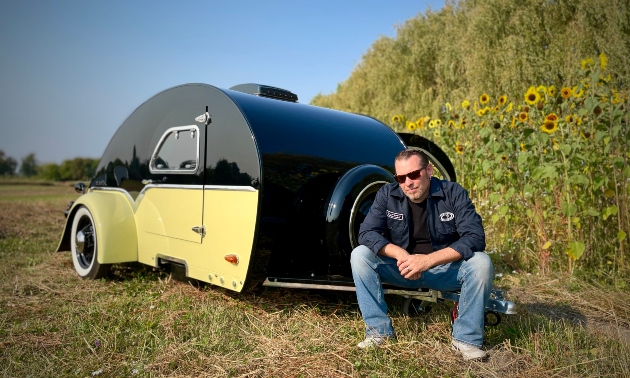 Jerry Clark sitting next to the yellow and black teardrop trailer he built from scratch