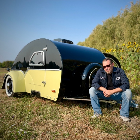 Jerry Clark sitting next to the yellow and black teardrop trailer he built from scratch