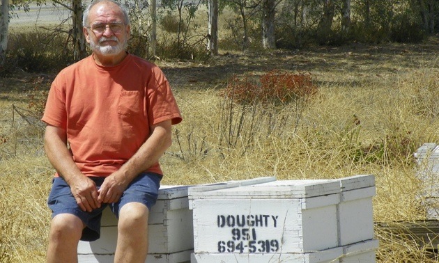 John Doughty sitting on some boxes of honey from his bees.