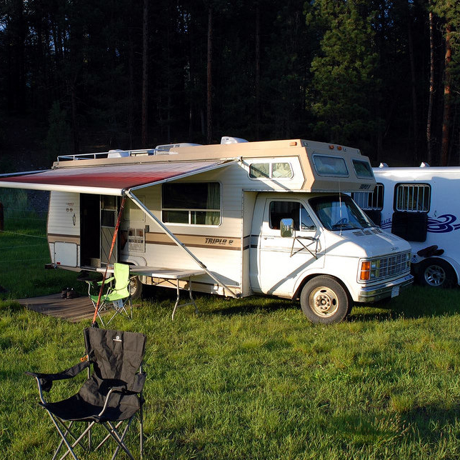 RV set up with a chair in front and two horses in the nearby pasture.