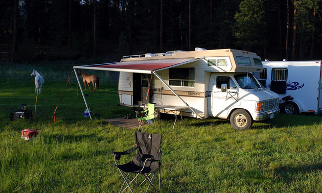 RV set up with a chair in front and two horses in the nearby pasture.