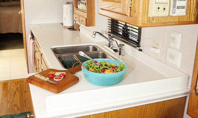 A photo of an RV kitchen with a salad and cutting board in the countertop. 