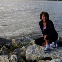 Photo of Laurie Oughton sitting on the rocks in front of a lake.