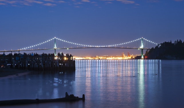 Lions Gate Bridge at night with lights reflecting in the water