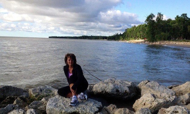 Photo of Laurie Oughton sitting on the rocks in front of a lake.