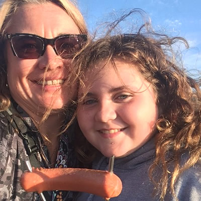 Mom and girl holding up hot dog on stick. 