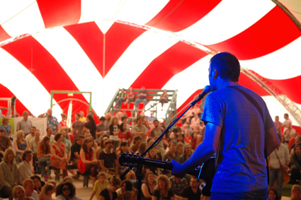 Musician plays in front of crowd under a tent