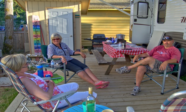 3 friends sitting in lawn chairs on a deck in front of an RV.