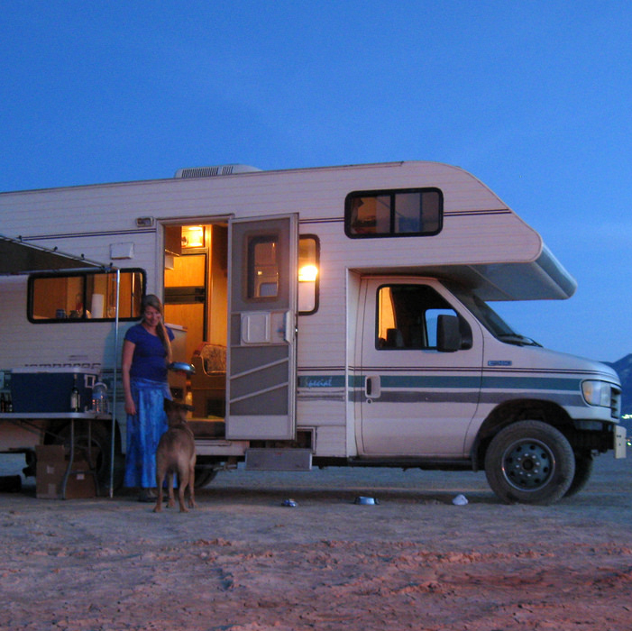 RV at an RV park with a smiling lady and her dog standing in front