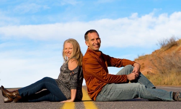 Julie and Marc sitting back to back with blue sky behind them